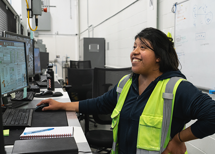 Salma smiles while standing at a desk 