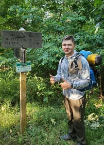 Peter stands with sign while hiking